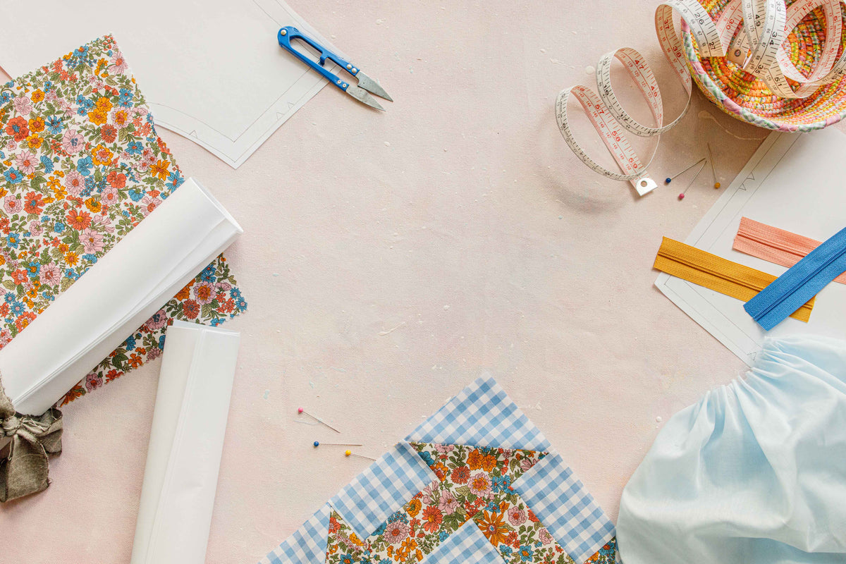 a styled flat lay of printed sewing patterns rolled up with an assortment of sewing tools and projecjts on a backdrop