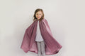 Smiling small girl standing in front of a white studio backdrop wearing 208 Kinsale Cloak for Young Maidens arms extended to either side to display the voluminous cloak.