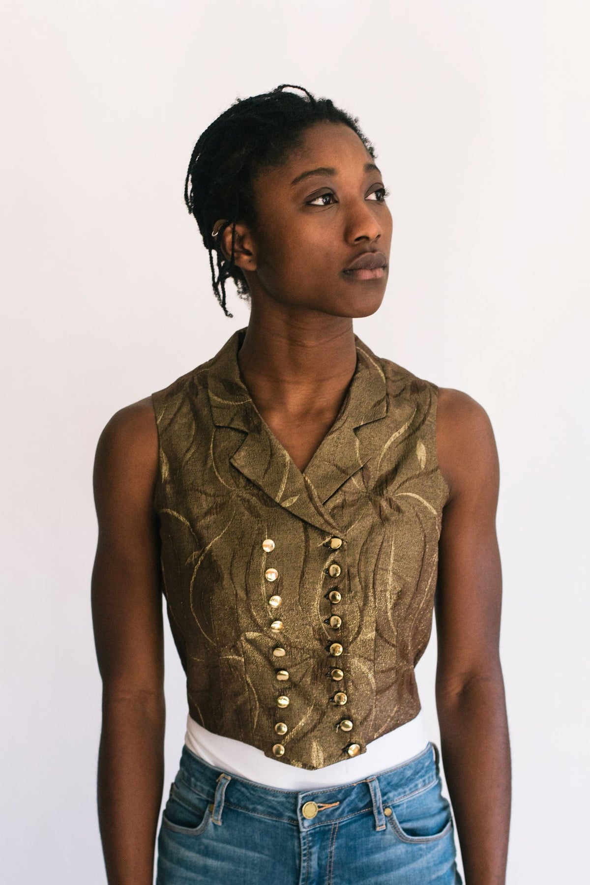 Young African woman standing in front of a white studio back drop looking to the right wearing View C 222 Vintage Vests. With small notched collar plunging into the double breasted front, which closes with two rows of buttons.
